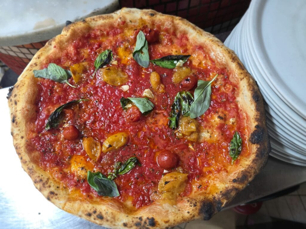 Pizza marinara con aglio di Voghiera DOP, pomodorini San Marzano e gialli del Piennolo e basilico fresco, appena uscita dal forno a legna